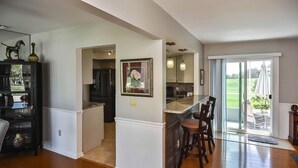 A modern kitchen with a central island, a dining area with bar stools, and a sliding glass door leading to a patio. - Burnt Store Isles Golf Home, W/Hot Tub/King Bed/Fast WIFI/Unbeatable Location (Punta Gorda)