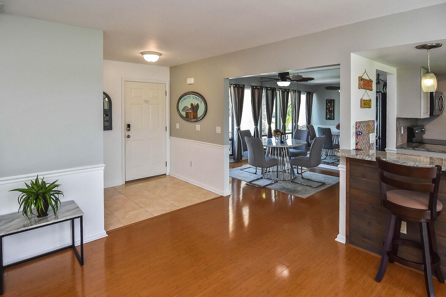 A spacious living area with a dining table and chairs, a kitchen with a bar, and a hallway leading to a door.