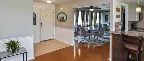 A spacious living area with a dining table and chairs, a kitchen with a bar, and a hallway leading to a door.