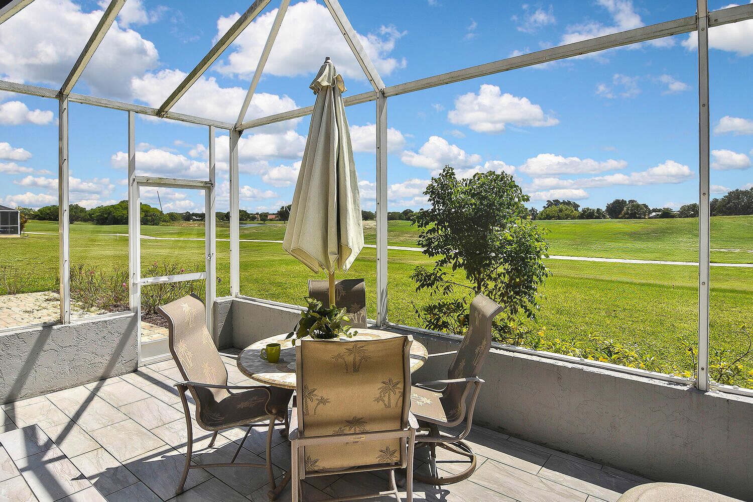 Une terrasse couverte, avec une table et des chaises, donnant sur un champ verdoyant.