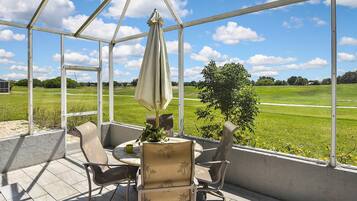 Une terrasse couverte, avec une table et des chaises, donnant sur un champ verdoyant.
