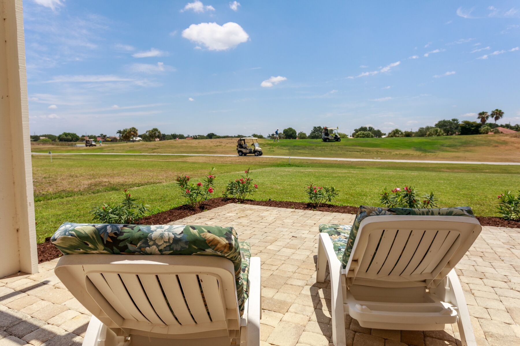 Two outdoor lounge chairs with a view of a golf course and a clear sky.