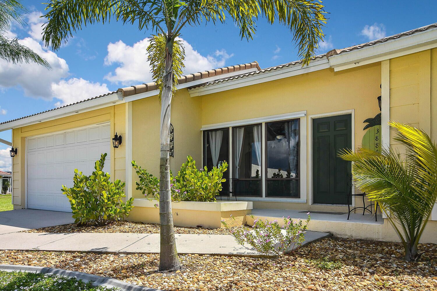 A yellow building with a garage, large windows, and a small patio area with plants.
