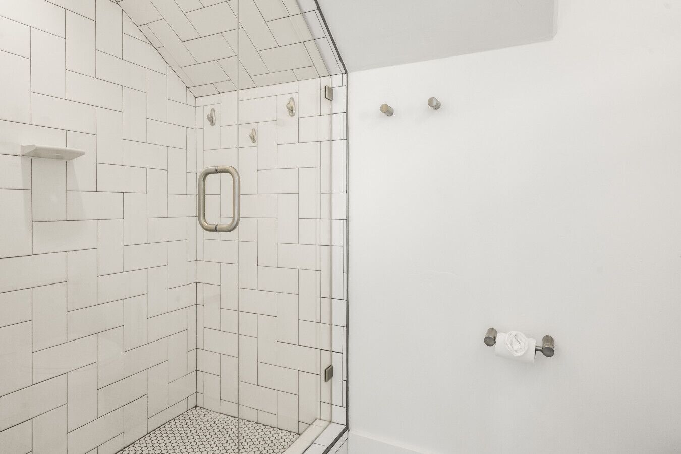 A white-tiled shower with a glass door, a metal grab bar, and a shower control panel.