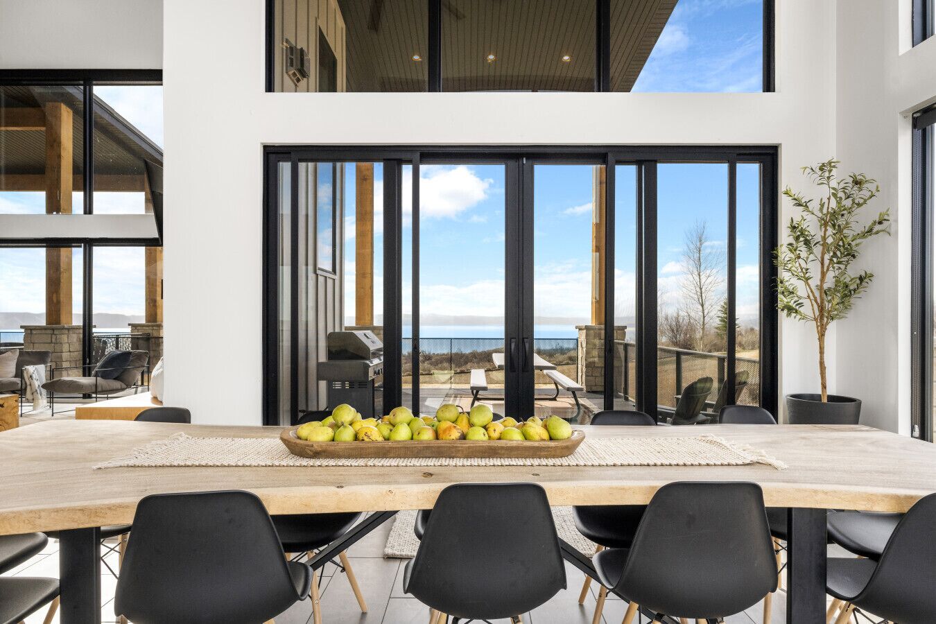 A modern dining area with a large table, black chairs, and a bowl of fruit.