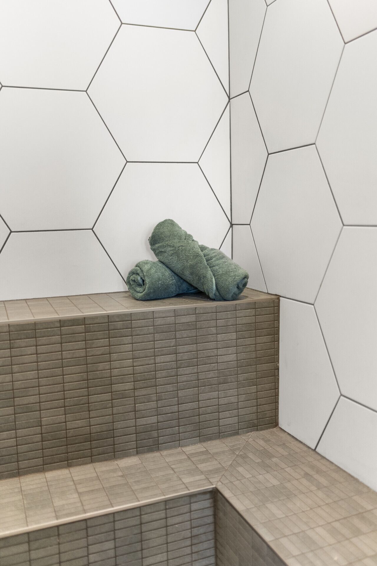 Et badeværelse med vægge i et hexagonmønster, en flisebelagt bænk og et sammenrullet håndklæde på bænken.