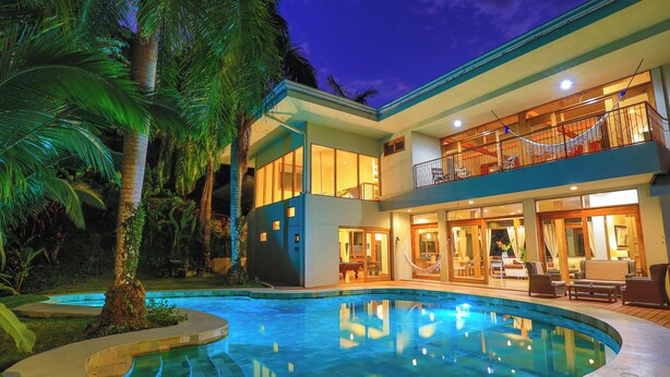 Une maison à deux étages avec une piscine, de grandes fenêtres et un espace salon extérieur.
