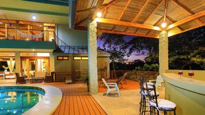 Un espace aménagé au bord de la piscine, avec une terrasse en bois, des chaises longues et un bar doté de tabourets.