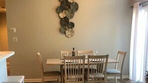 Un comedor con una mesa y sillas de madera, un adorno en la pared y una ventana con cortinas.