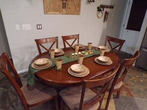 Een ronde houten eettafel gedekt met borden, kommen en kopjes, omringd door houten stoelen.