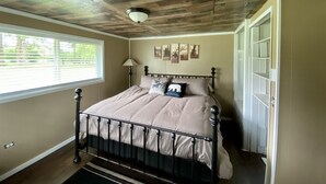Une chambre avec un plafond en bois, un lit avec un cadre en métal, une fenêtre avec des stores et une porte.
