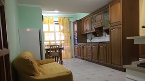 Una cocina compacta con armarios de madera, una mesa de comedor con sillas y un sillón amarillo.