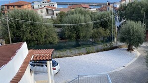 Un barrio residencial con un coche blanco estacionado en una calle empedrada, rodeado de árboles y edificios con tejados de tejas rojas.