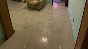 Una habitación amplia con un sillón estampado, piso de baldosas y una puerta que da a otra estancia.