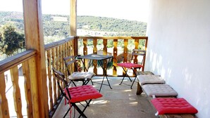 Ein Balkon mit Holzgeländer, einem Tisch, zwei Stühlen und einer Bank mit Kissen.