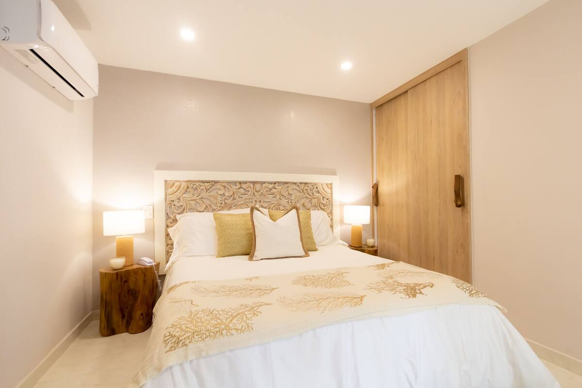 Een net opgemaakt bed met een bedsprei met patroon, twee nachtlampjes en een houten hoofdbord.