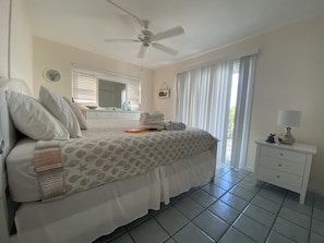 A bedroom with a bed, a nightstand, a ceiling fan, a window with blinds, and a view of greenery outside. - Walk to Siesta Key Beach & Village – Cozy 2BR , 1BA first floor (Sarasota)