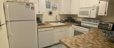 A compact kitchen with white cabinets, a refrigerator, a microwave, a stove, and a dishwasher.