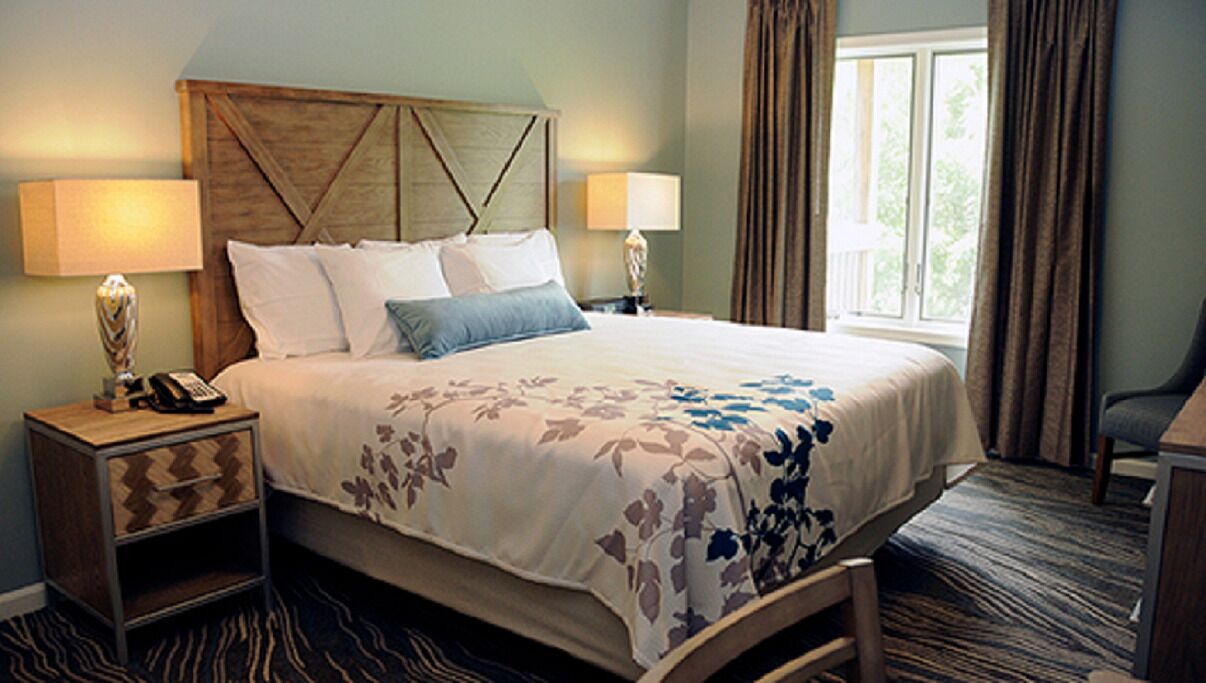A hotel room with a large bed, two bedside tables with lamps, a chair, and a window with curtains.