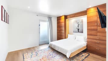 A bedroom with a bed, wooden wardrobe, and a colorful rug.