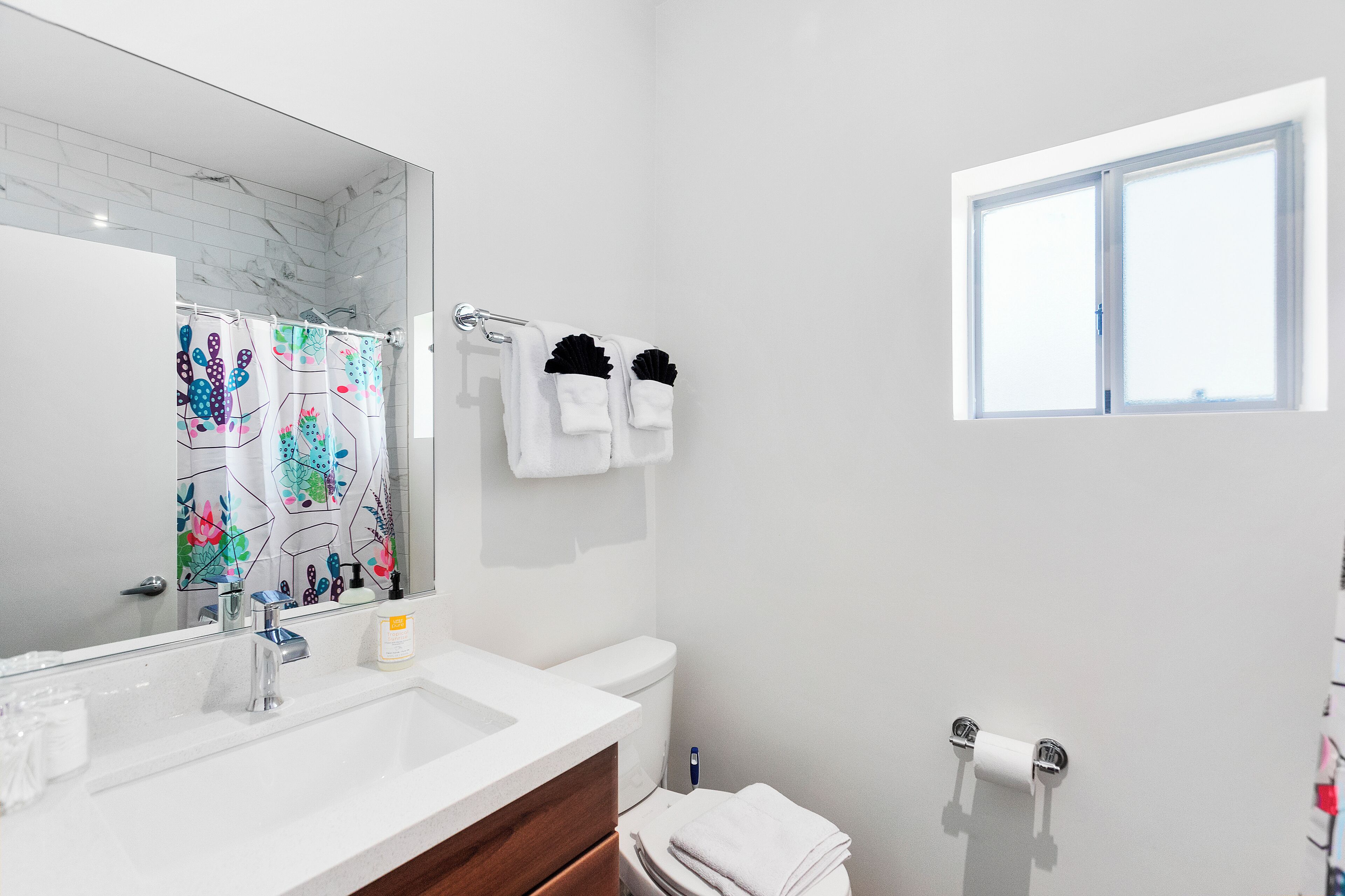 A bathroom with a white sink, a mirror, a toilet, and a window.