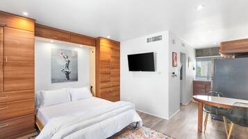 Una habitación de hotel moderna con una cama grande, un armario de madera, un televisor de pantalla plana y una pequeña zona de cocina.