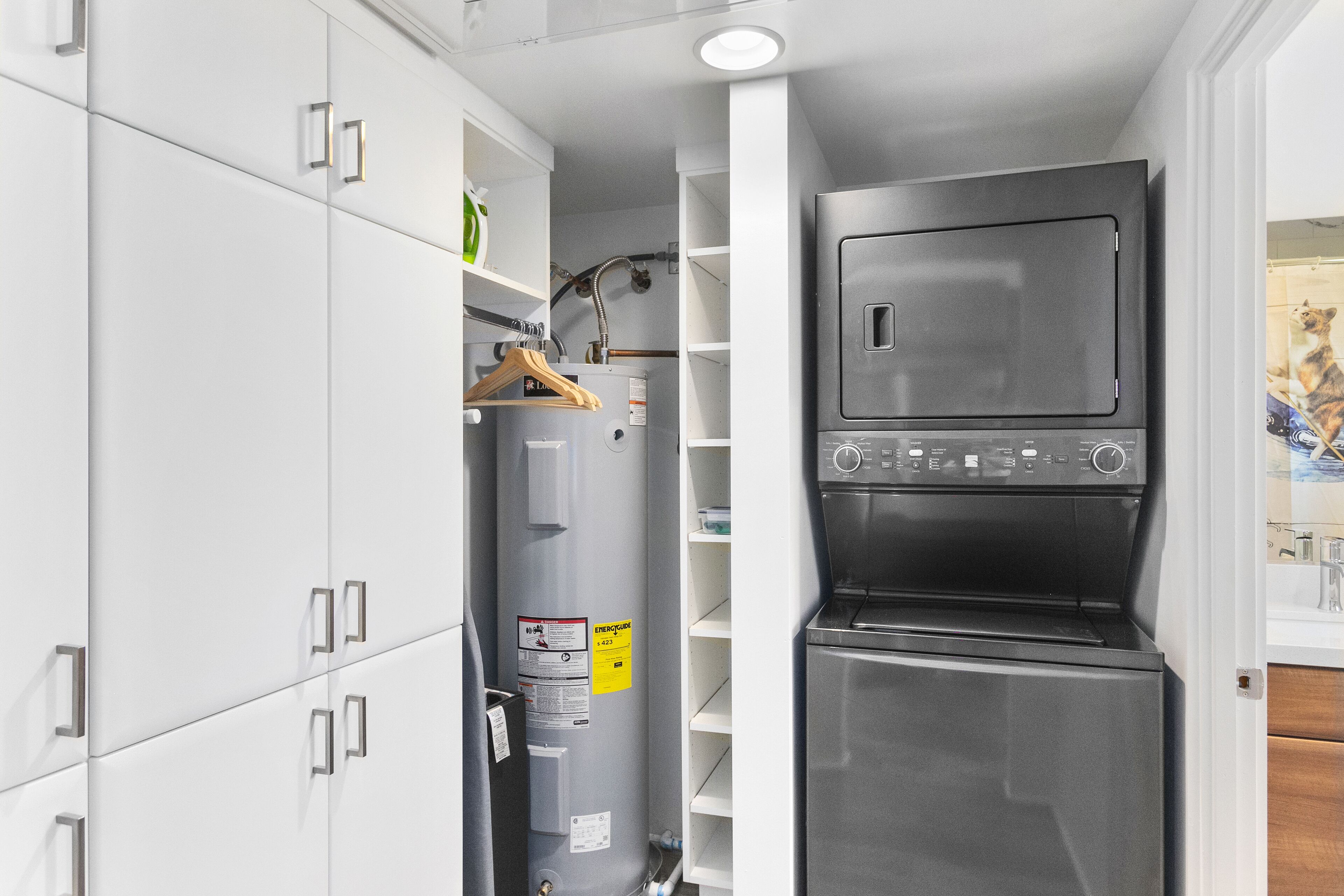 A compact kitchen with a built-in washer and dryer, white cabinetry, and a wooden hanger rack.