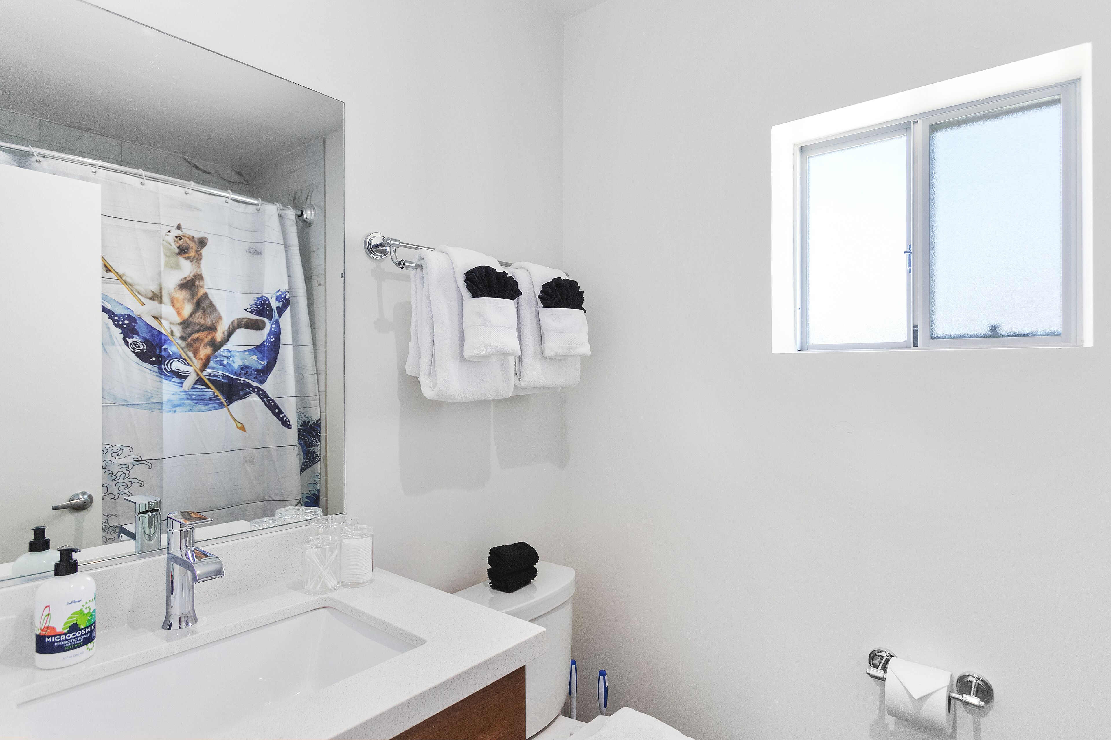 A modern bathroom with a white sink, a mirror, a toilet, and a window.