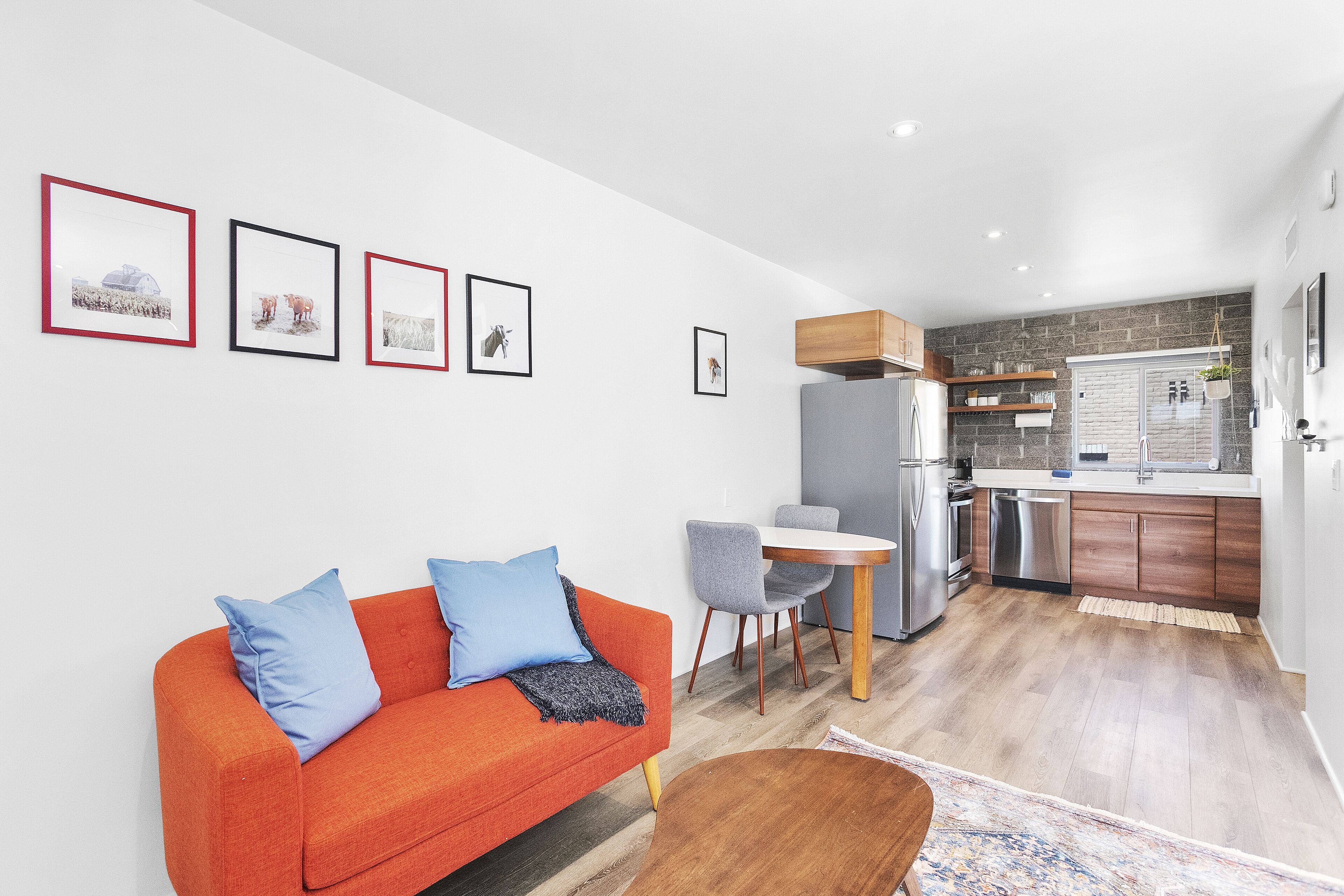 A modern living room with a sofa, a dining table, and a kitchen area with a refrigerator and wooden cabinets.
