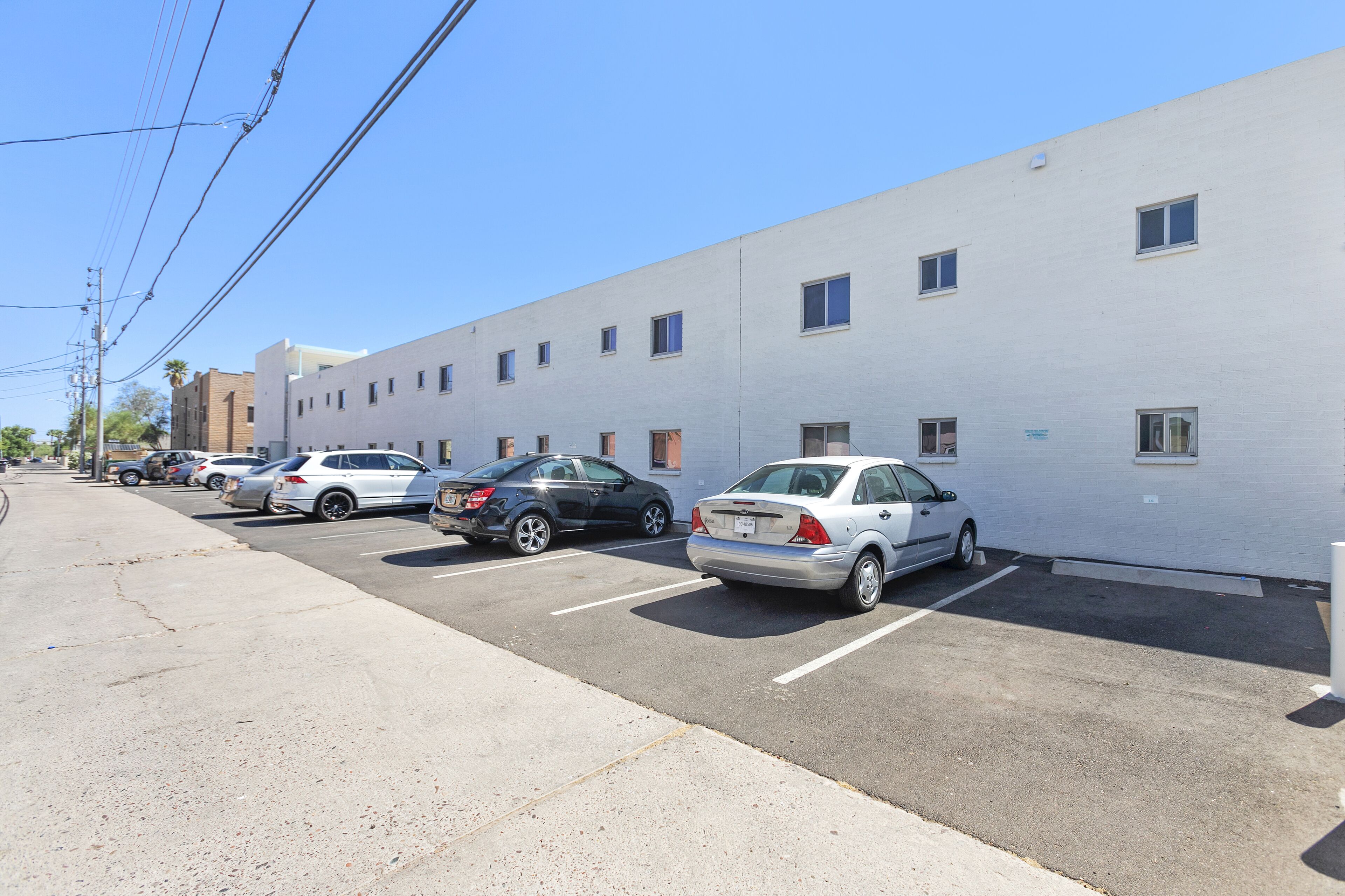 A parking lot with several cars parked in front of a white building with multiple windows.