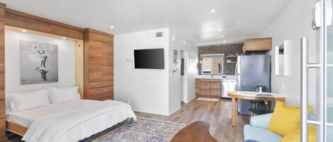 A modern bedroom with a large bed, a sitting area with a sofa, and a kitchen in the background.