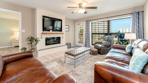 A living room with a fireplace, leather sofas, a flat-screen TV, and a balcony with a view of high-rise buildings. - Saida IV 407 - Ocean Front, Recently Updated, 3 Pools, Palapa Bar, Incredible Balcony Views (South Padre Island)
