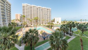 A hotel with a large pool, palm trees, and a view of the ocean. - Saida IV 407 - Ocean Front, Recently Updated, 3 Pools, Palapa Bar, Incredible Balcony Views (South Padre Island)