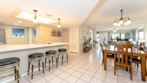 A spacious kitchen with a central island, bar stools, and a dining area with wooden chairs and a table. - Saida IV 407 - Ocean Front, Recently Updated, 3 Pools, Palapa Bar, Incredible Balcony Views (South Padre Island)