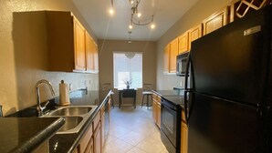 A kitchen with wooden cabinets, a black refrigerator, a stainless steel sink, and a chandelier.