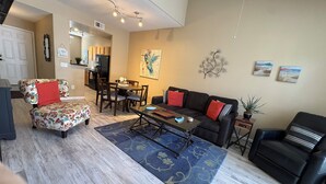 A living room with a sofa, armchair, coffee table, and a dining area with chairs and a table.
