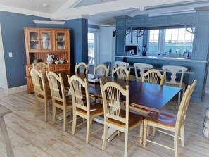 A dining area with a wooden table and chairs, a kitchen with blue cabinets, and a view of the sea through large windows.