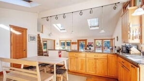 Een moderne keuken met houten kastjes, een eettafel met stoelen, hanglampen en dakramen.