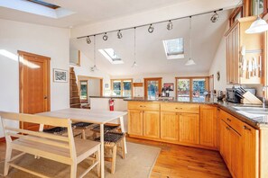 Eine moderne Küche mit Holzschränken, einem Esstisch mit Stühlen, Pendelleuchten und Dachfenstern.