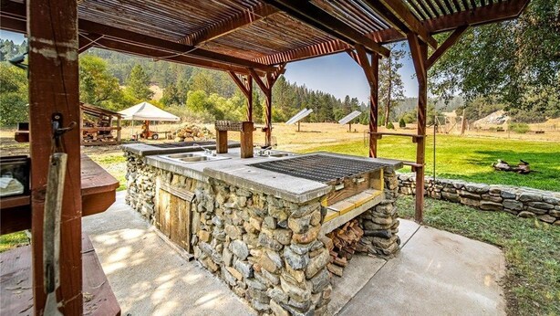 Een steen barbecueplaats met een houten pergola, zonnepanelen en een stenen muur.
