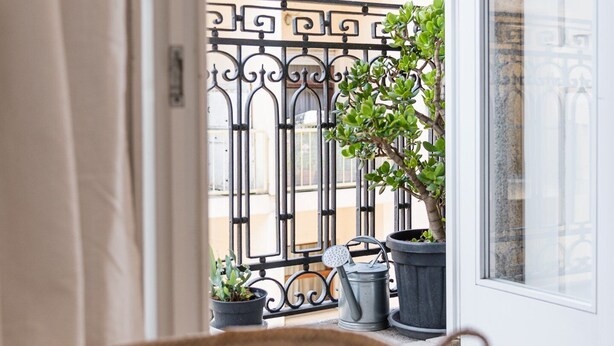 Een balkon met een ijzeren hekwerk, bloempotten en een rieten stoel.