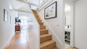 Een modern interieur met een houten trap, witte muren en een gang naar een kamer met uitzicht.