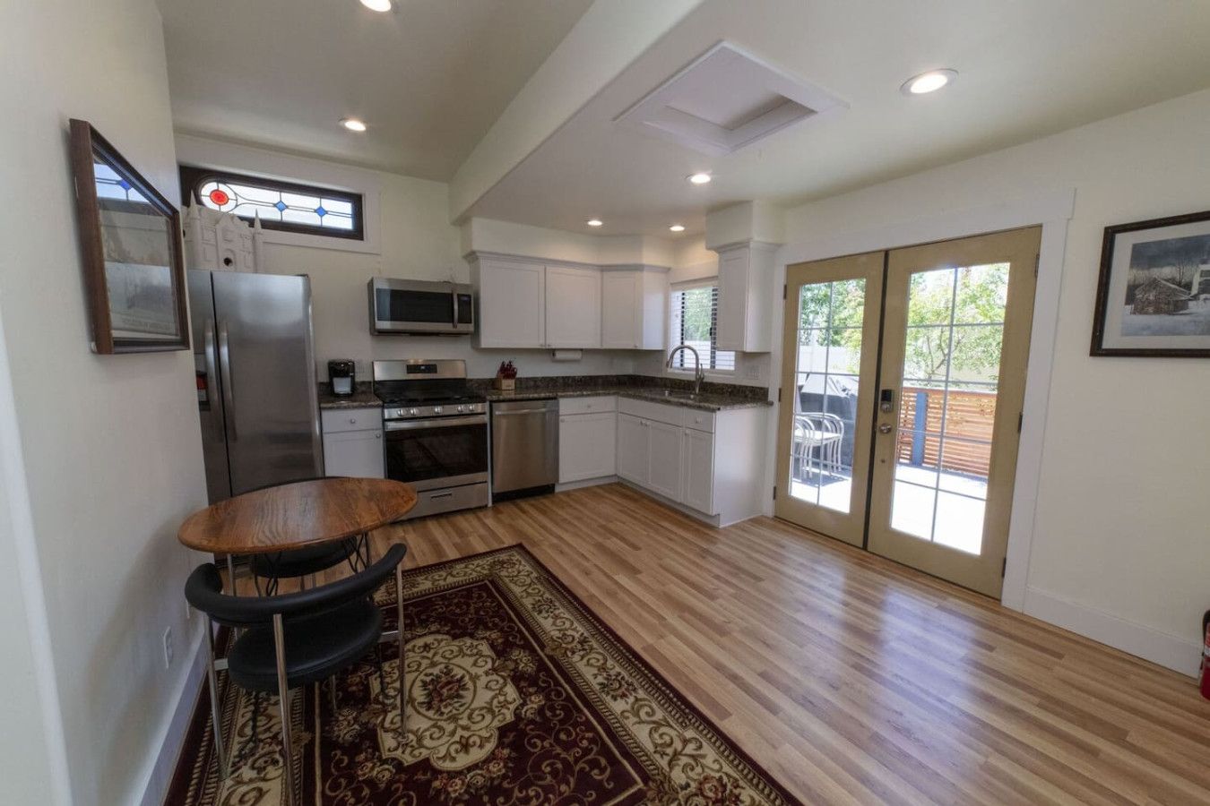 A modern kitchen with white cabinets, stainless steel appliances, and a dining area with a wooden table and chairs.