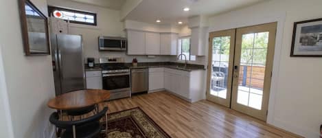 A modern kitchen with white cabinets, stainless steel appliances, and a dining area with a wooden table and chairs.