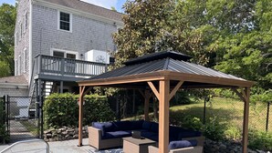 Een overdekt terras met een pergola, beklede banken en een kamerkleed met dessin.