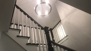 Een trap met witte spijlen en een zwarte leuning, die uitkomt op een vloer met een ronde lamp.
