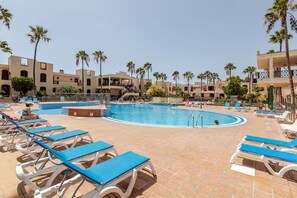 A resort pool area with multiple swimming pools, lounge chairs, and palm trees. - Spacious, bright studio with a terrace and a view of the pool (Arona)