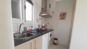 A small kitchen with a sink, a stove, and a trash bin.