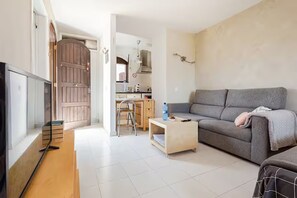 A living room with a grey sofa, a wooden coffee table, and a TV. There's a kitchen area with a stove and cabinets. - Spacious, bright studio with a terrace and a view of the pool (Arona)