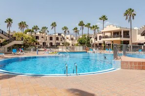 A swimming pool with lounge chairs and palm trees. - Spacious, bright studio with a terrace and a view of the pool (Arona)
